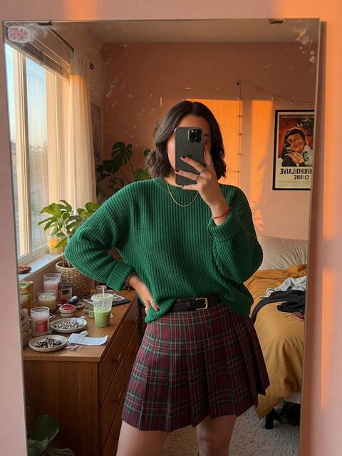 A mirror selfie in a green knit sweater and a plaid pleated skirt