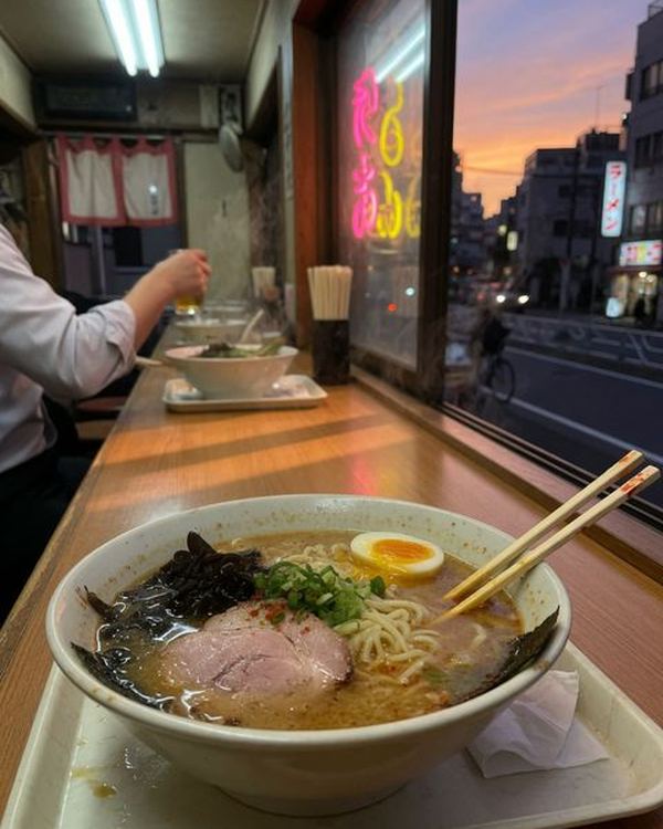 A bowl of ramen with a soft-boiled egg, chashu and nori on a window counter at dusk